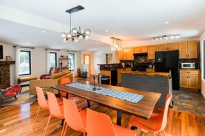 Une cuisine moderne avec des meubles en bois, un îlot central et un coin repas comprenant une table en bois et des chaises orange.