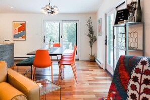 Un espace repas moderne avec un plancher en bois, une table noire et des chaises orange.