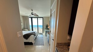 A hotel room with a bed, a ceiling fan, a view of the ocean, and a kitchen area with a granite countertop. - Gulf Front Condo with Stunning Views! (Pensacola)