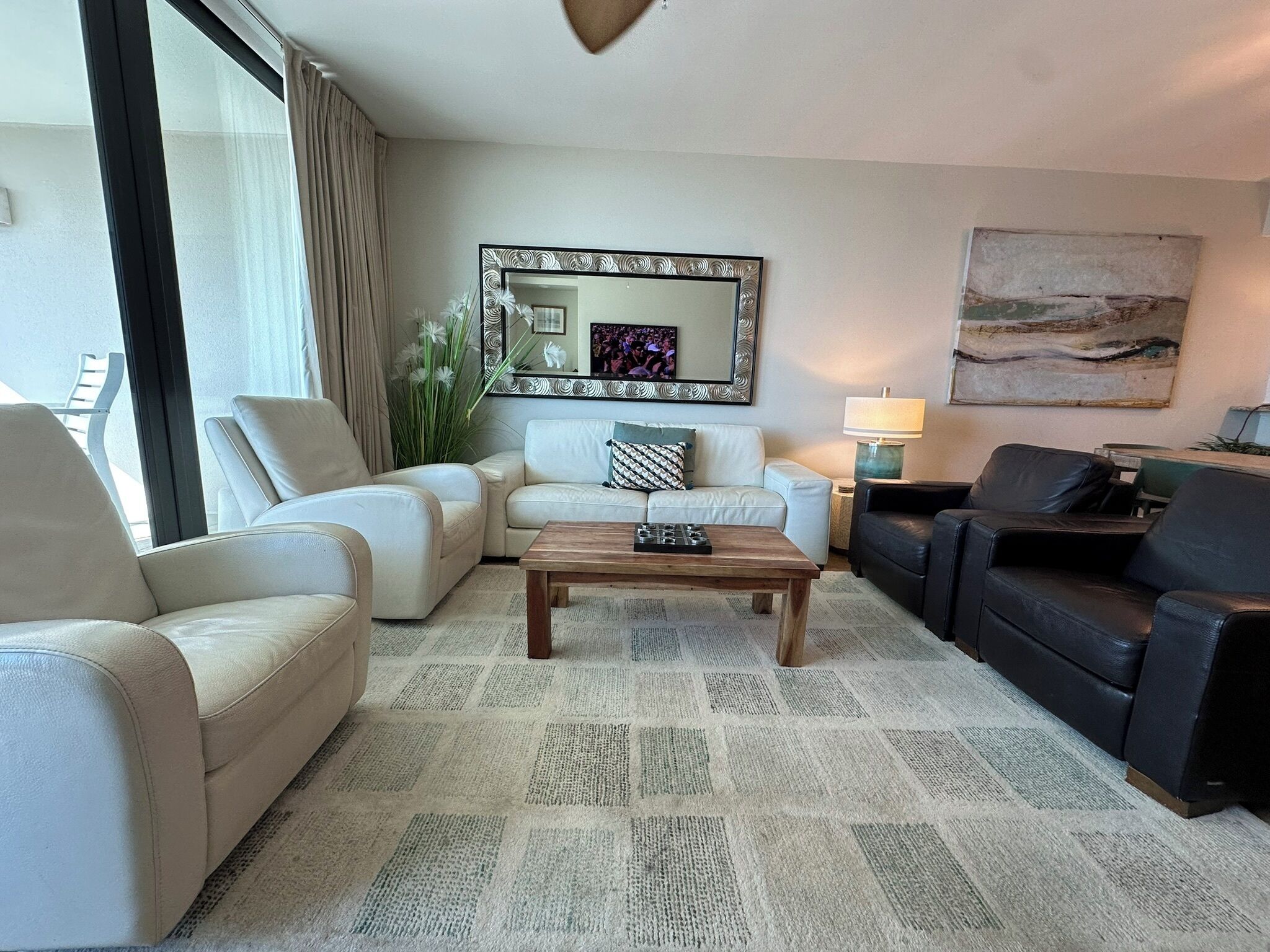 Un salon comprenant un canapé, des fauteuils, une table basse, un miroir, une lampe et un tableau accroché au mur.