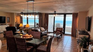 A spacious living area with a large dining table, comfortable seating, and a view of the ocean through large windows. - Gulf Front Condo with Stunning Views! (Pensacola)