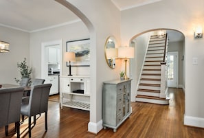 A spacious living room with a dining area, a staircase, and a kitchen visible through an archway. - Luxurious Cape Cod in Emerywood - Minutes to Furniture Market & HP University (High Point)