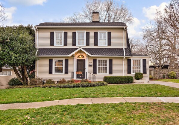 A two-story house with a front porch, a chimney, and a well-maintained lawn. - Luxurious Cape Cod in Emerywood - Minutes to Furniture Market & HP University (High Point)