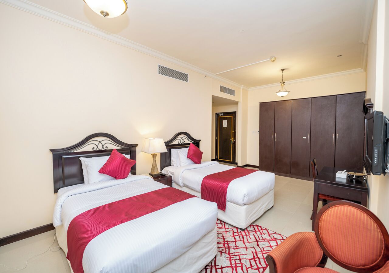 Ein Hotelzimmer mit zwei Betten, einem Schreibtisch, einem Sessel und einem Fernseher.