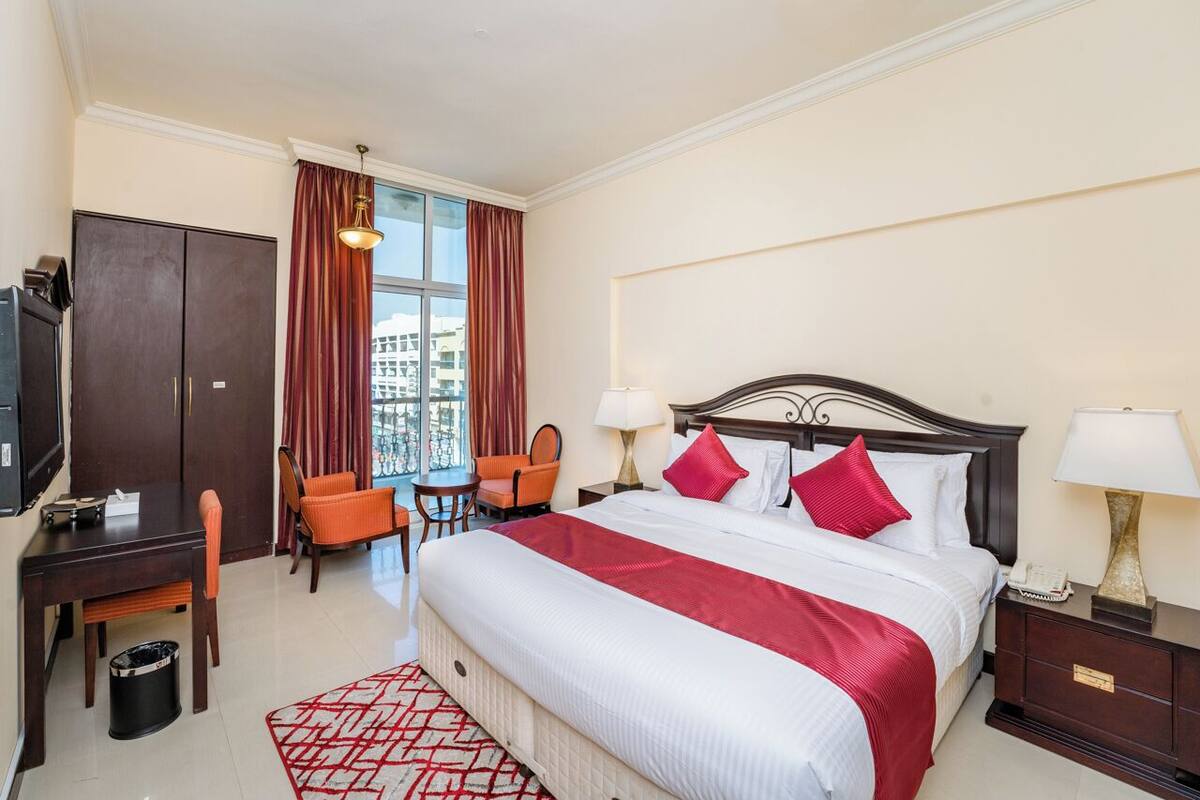 A hotel room with a large bed, a desk, a chair, a wardrobe, and a window with curtains.