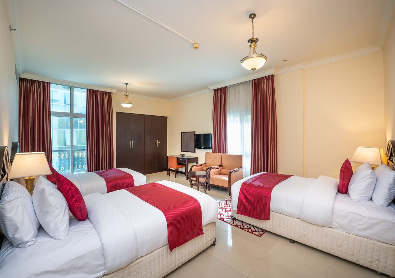 Ein Hotelzimmer mit zwei Betten, einem Schreibtisch, einem Sessel und einem Fernseher.