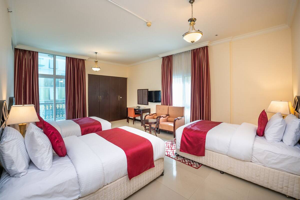 A hotel room with two beds, a desk, a chair, and a TV.