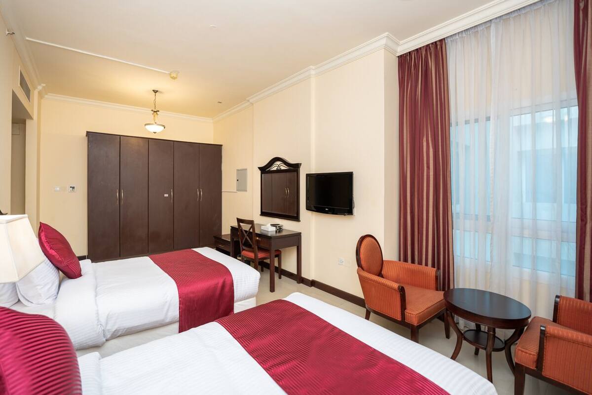 A hotel room with two beds, a desk, a chair, a television, and a large window with curtains.