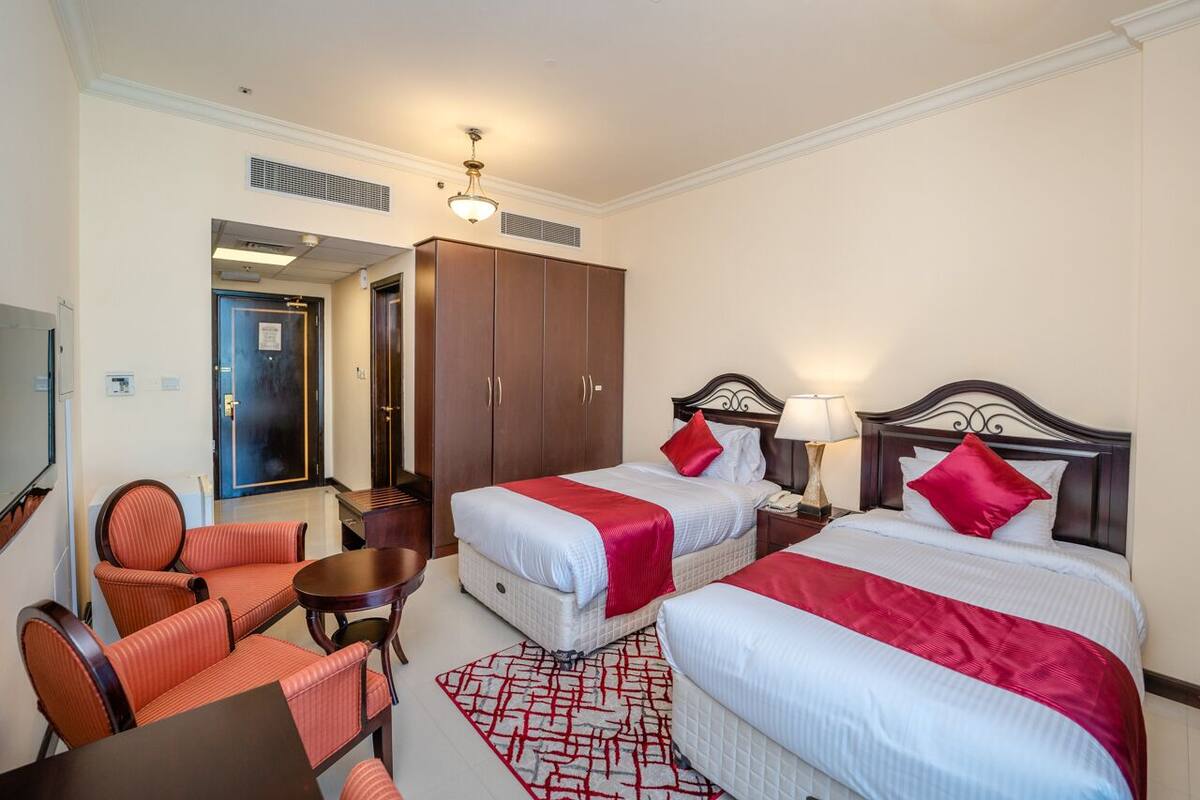 A hotel room with two beds, a desk, a chair, and a TV.