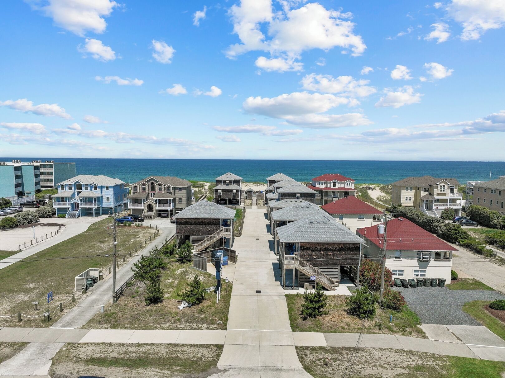 Un quartier résidentiel situé sur la côte, avec de nombreuses maisons à deux étages, une plage en arrière-plan et un ciel dégagé.