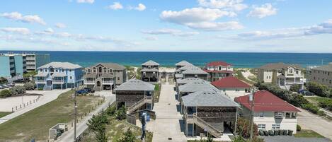 Un quartier résidentiel situé sur la côte, avec de nombreuses maisons à deux étages, une plage en arrière-plan et un ciel dégagé.