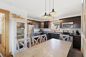 A modern kitchen with dark wood cabinets, stainless steel appliances, and a wooden dining table.