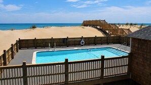 Ein Schwimmbad mit Holzterrasse, Holzzaun und Blick auf Strand und Meer.