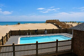 Une piscine avec une terrasse en bois, une clôture en bois et une vue sur la plage et l’océan.