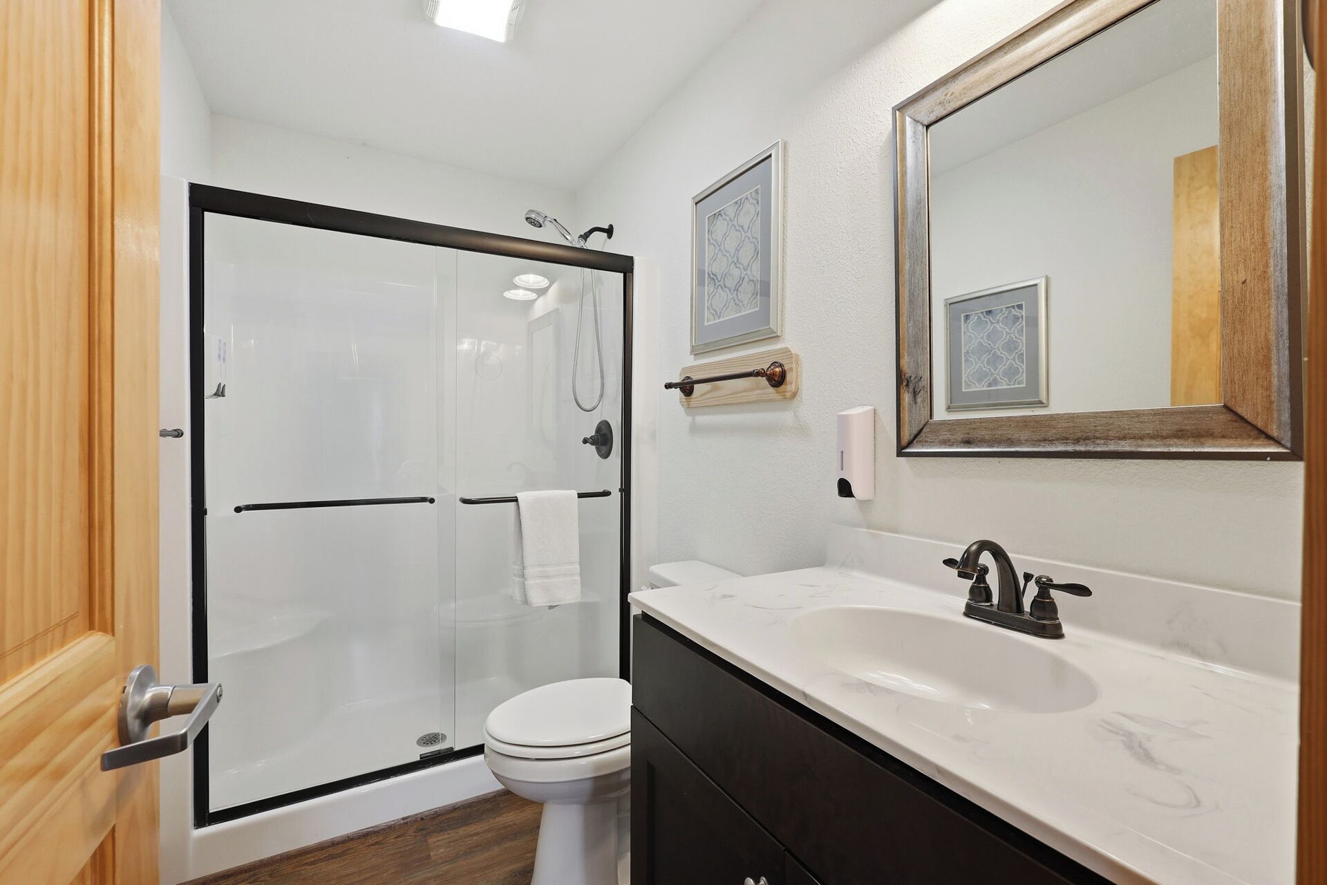 A bathroom with a glass-enclosed shower, a white toilet, a sink with a faucet, and a mirror with a wooden frame.
