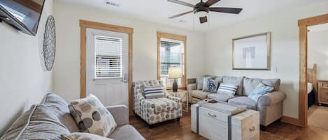 Una sala de estar con sofá, sillón, reposapiés y ventilador de techo.