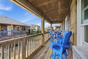 Une terrasse en bois avec des chaises bleues, un espace abrité et une vue sur les maisons voisines.