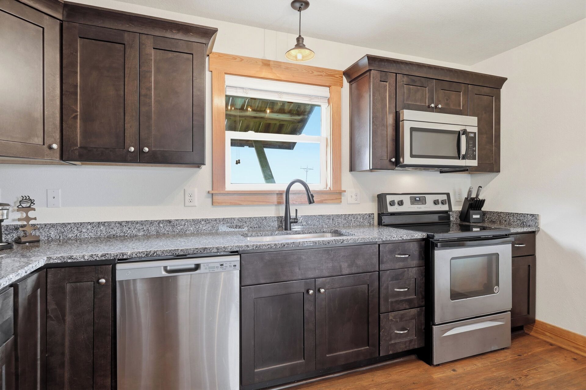 A kitchen with dark wooden cabinets, stainless steel appliances, a granite countertop, and a window with a view.
