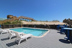 Uma área de piscina com deck de madeira, espreguiçadeiras e mesas.
