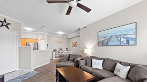 A modern living room with a grey sofa set, a wooden coffee table, and a ceiling fan. - Salty But Sweet at Sundune Village, Located 0.1 Miles from the Beach! (Kill Devil Hills)