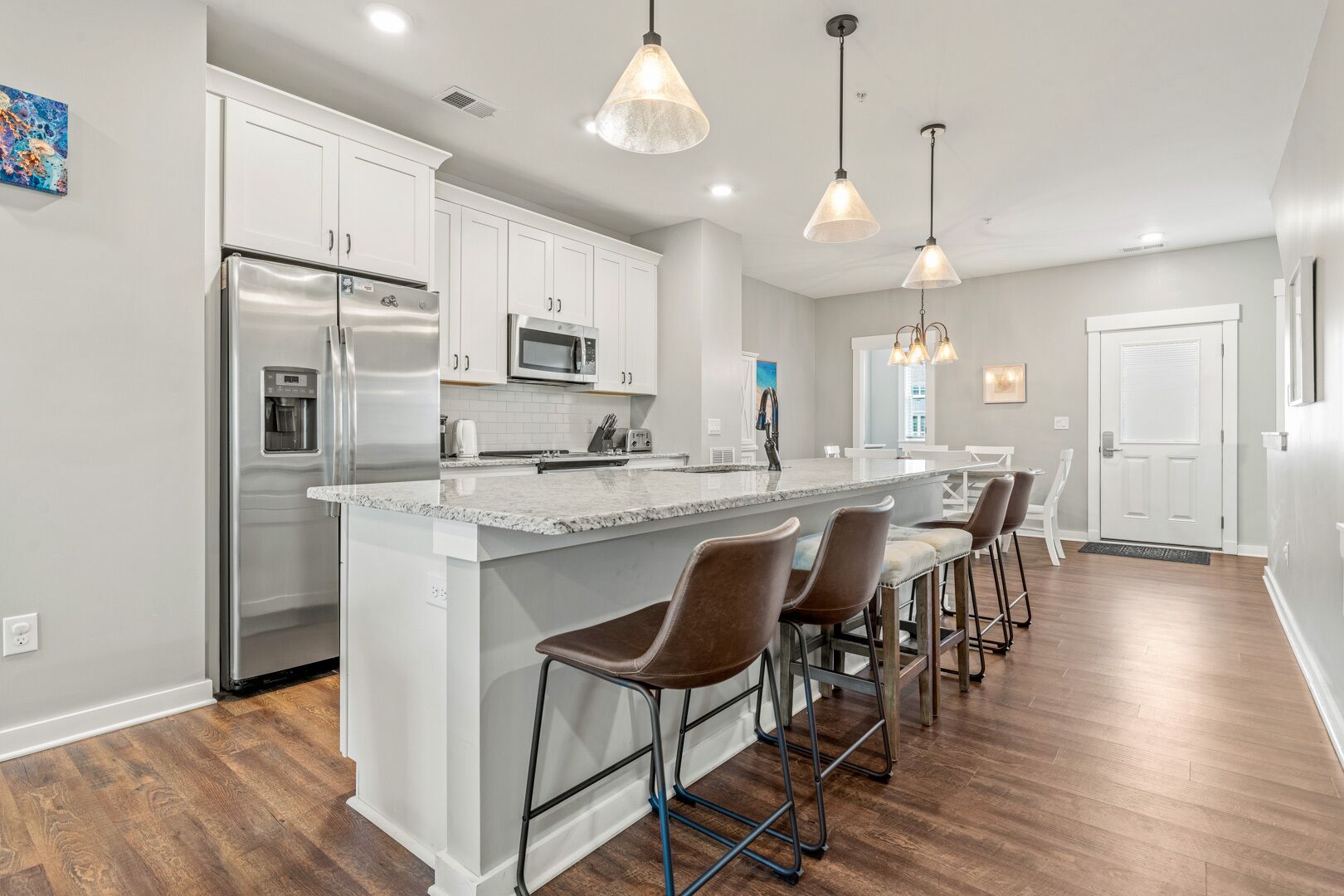 A modern kitchen with white cabinets, stainless steel appliances, a granite countertop, and a bar area with stools.