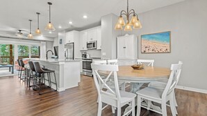 A modern kitchen with white cabinets, a central island, and a dining area with a round table and white chairs.