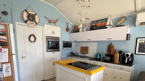 A compact kitchen with a central island, white cabinets, and a blue wall. - Family Friendly Shack with Bay Views (Fisherman bay)