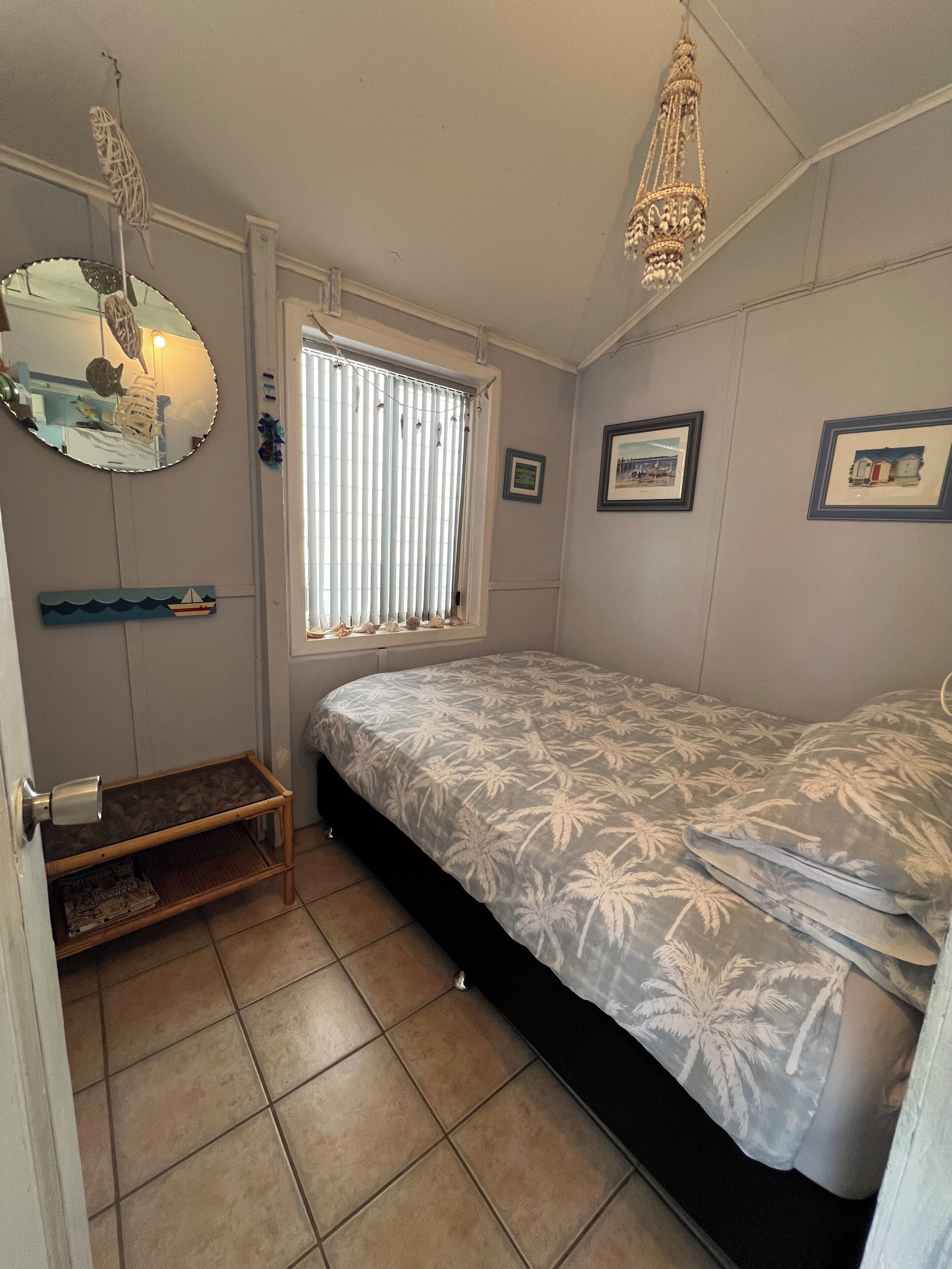 Ein Schlafzimmer mit einem Bett, einem Fenster mit Jalousien, einem Spiegel und einer Deckenleuchte.
