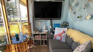 A living room with a sofa, a television, a bookshelf, and a dining area with chairs and a table. - Family Friendly Shack with Bay Views (Fisherman bay)