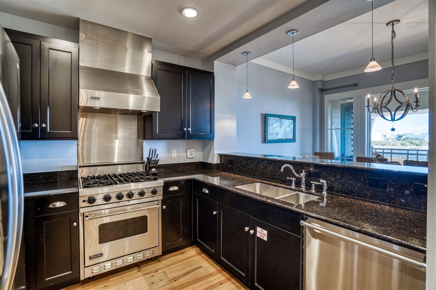 A modern kitchen with stainless steel appliances, black cabinets, granite countertops, and pendant lighting.