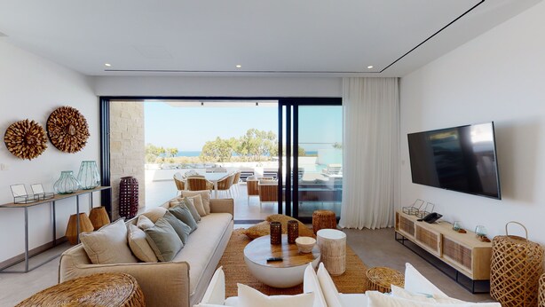 A modern living room with a sofa, coffee table, and TV. It features a large window with a view of the ocean. - Periyiali Resort , Villa Melpomeni 21 at Konnos Beach - Cape Greco (Paralimni-Protaras)