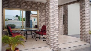A modern outdoor patio with a glass table and red chairs, surrounded by textured stone walls and a view of the neighborhood. - Gated Community (Lashibi, Tema)