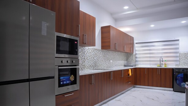 A modern kitchen with stainless steel appliances, wooden cabinets, and a tiled backsplash. - Gated Community (Lashibi, Tema)