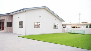 A modern two-story house with a flat roof, a covered porch, and a well-maintained lawn. - Gated Community (Lashibi, Tema)