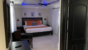 Una habitació d'hotel amb llit, escriptori, cadira, ventilador de sostre i una porta.