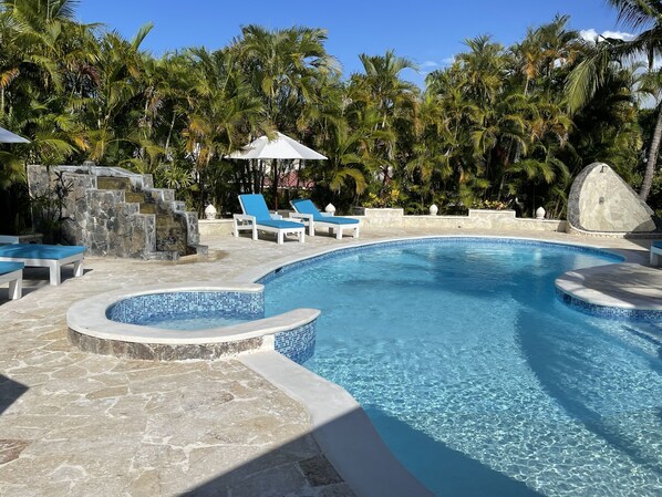 A swimming pool with clear water, surrounded by stone tiles and blue lounge chairs.