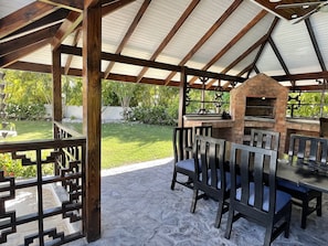 An outdoor patio with a brick oven, wooden chairs, and a table.