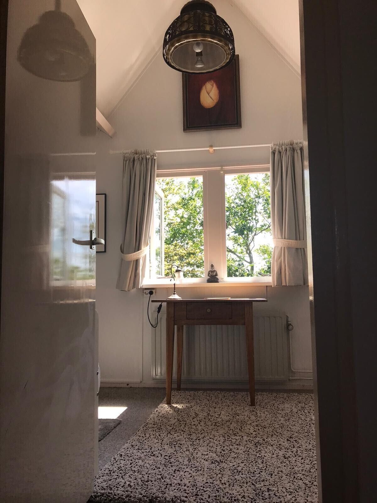 Une pièce avec une table en bois, une fenêtre avec des rideaux, une horloge murale et un radiateur.