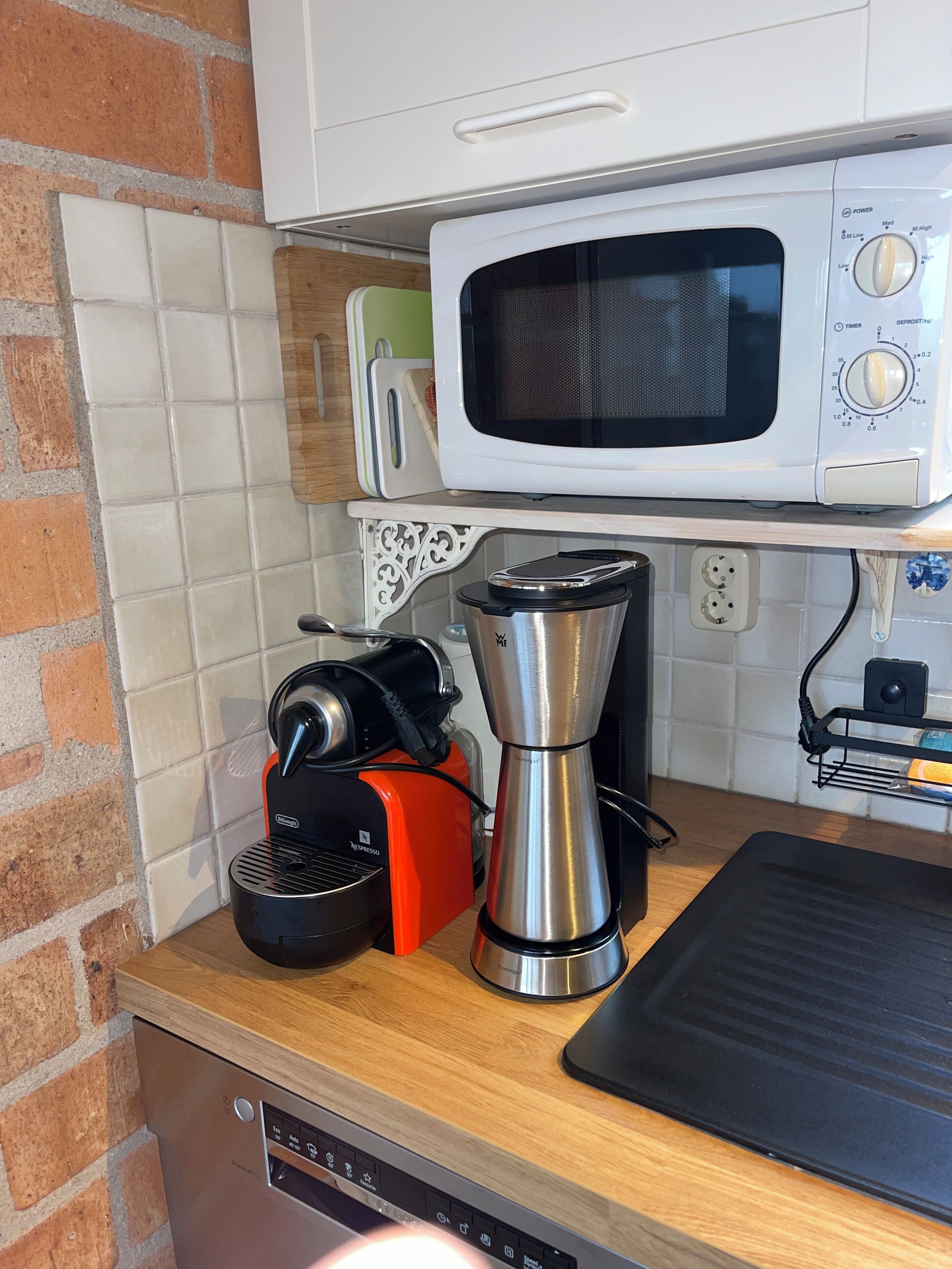 A kitchen with a microwave, coffee maker, and espresso machine on a wooden countertop.