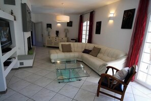A living room with a sectional sofa, a glass coffee table, a TV, and a fireplace. - Perfect villa with pool - fantastic location A3693 (Lège-Cap-Ferret)