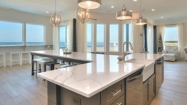 A modern kitchen with a large island, pendant lighting, and large windows offering ocean views.
