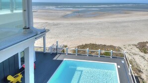 A poolside view with a clear ocean view, a wooden deck, and a glass-enclosed area.