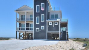 A two-story beachfront house with a balcony, a covered porch, and a staircase leading to the upper level.
