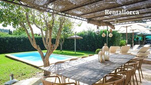 An outdoor dining area with a table and chairs, a pool, and a pergola with hanging lights. - Es Collet by Rentallorca (Manacor)