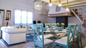 A spacious living room with a white sofa, teal chairs, and a glass dining table. There is a staircase leading to an upper level, and a chandelier hangs from the ceiling. - Es Collet by Rentallorca (Manacor)