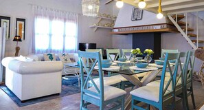A spacious living room with a white sofa, teal chairs, and a glass dining table. There is a staircase leading to an upper level, and a chandelier hangs from the ceiling. - Es Collet by Rentallorca (Manacor)