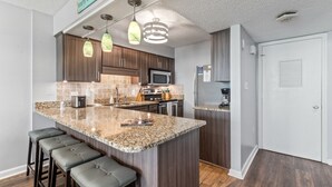 A modern kitchen with granite countertops, dark wood cabinets, and a central island with bar stools. - Crescent Sands In Windy Hill D6 3 Bedroom Condo by RedAwning (North Myrtle Beach)