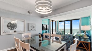 A dining area with a glass table, white chairs, and a view of the ocean. - Crescent Sands In Windy Hill D6 3 Bedroom Condo by RedAwning (North Myrtle Beach)