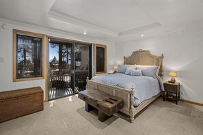 Un dormitorio con una cama grande, un banco, una mesita de noche y vistas a través de una puerta corrediza de vidrio.