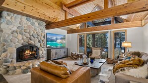 A cozy living room with a stone fireplace, leather furniture, and a large window overlooking a scenic view. - Lake View 2BR/2BA Incline Village w/ Fireplace (Incline Village)